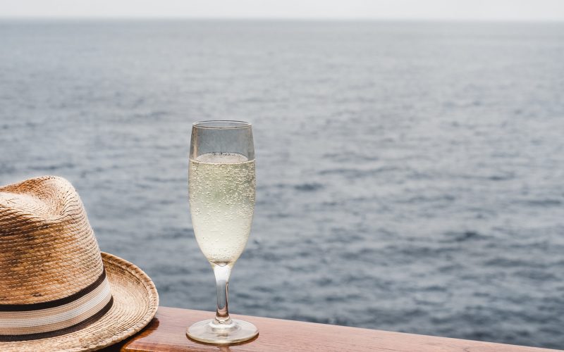 Beautiful champagne glass on the open deck of a cruise liner against the backdrop of blue sea waves. Side view, close-up. Concept of leisure and travel